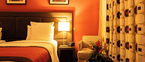 A hotel room with a bed, bedside table, lamp, chair, and a decorative vase.
