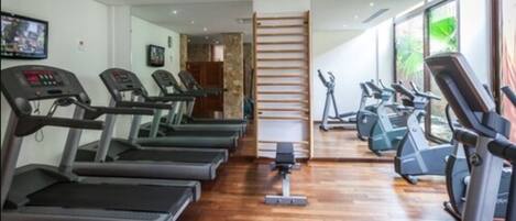 Un gimnasio con cintas de correr, elípticas y piso de madera.