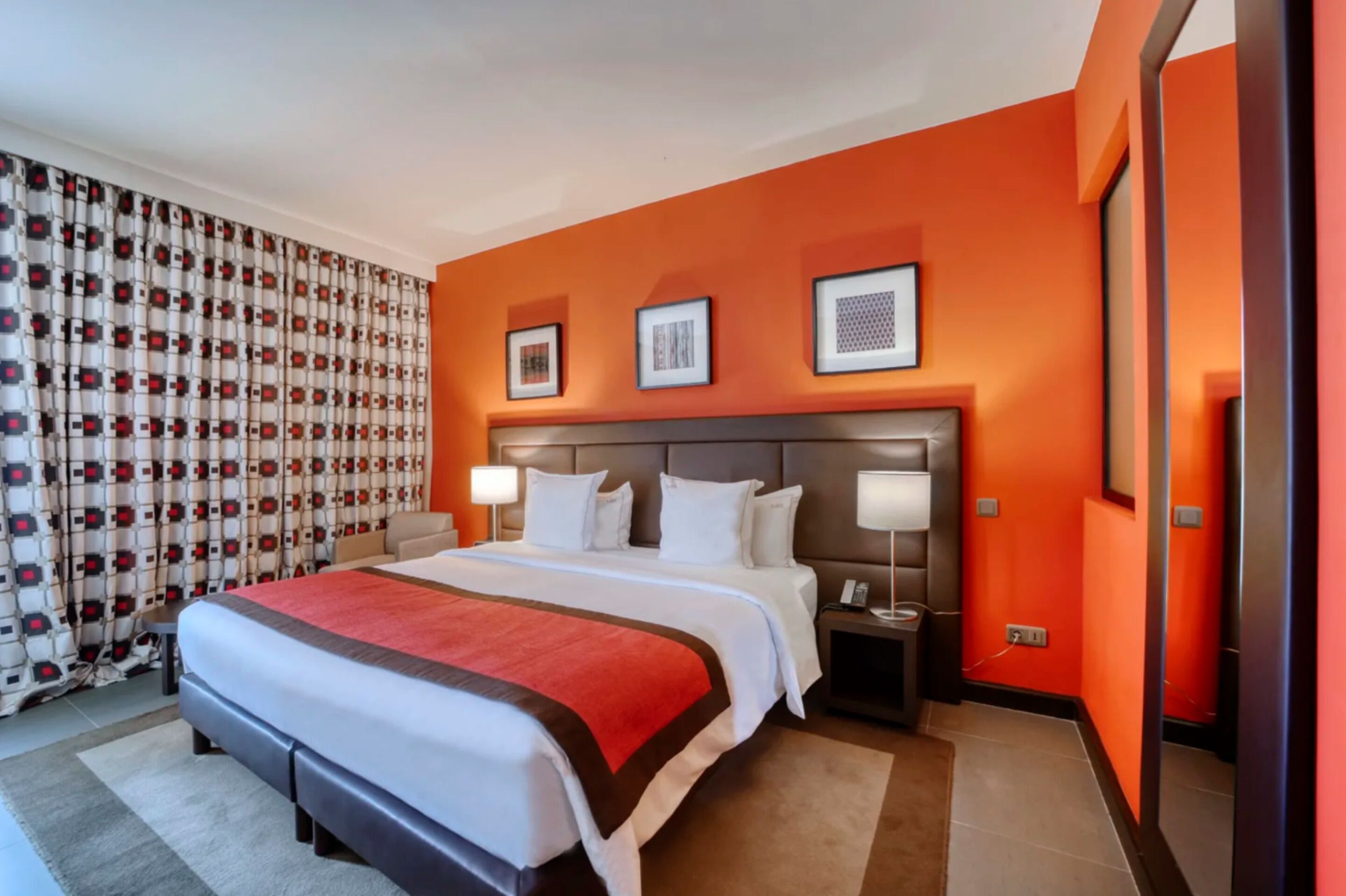 A hotel room with a large bed, two bedside tables with lamps, a headboard, and a mirror on the wall.