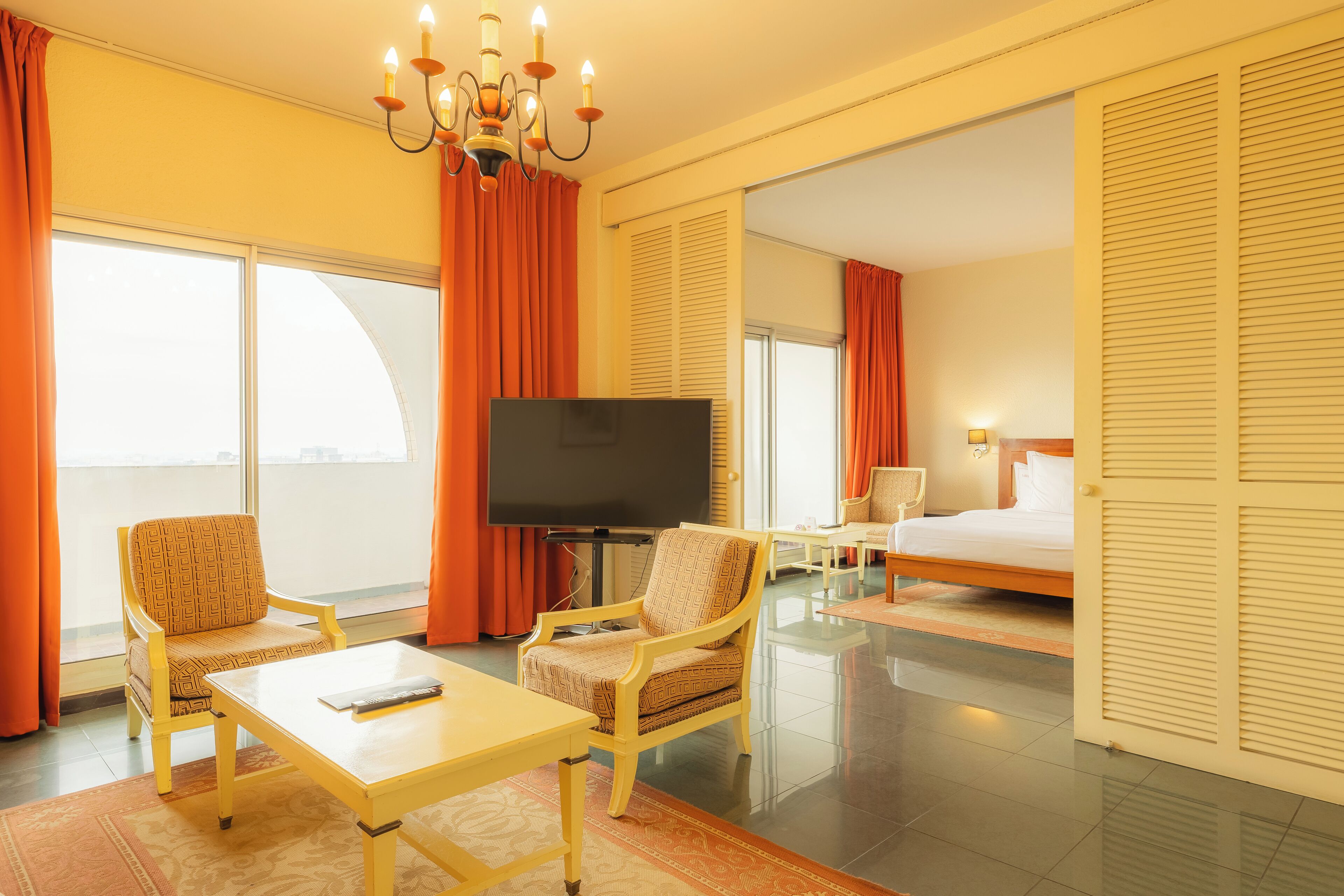 Una habitación de hotel con cama, dos sillones, televisión y un ventanal con cortinas.