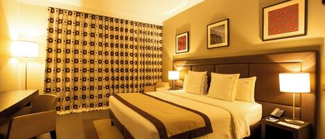 A hotel room with a large bed, bedside lamps, a desk, and a chair.