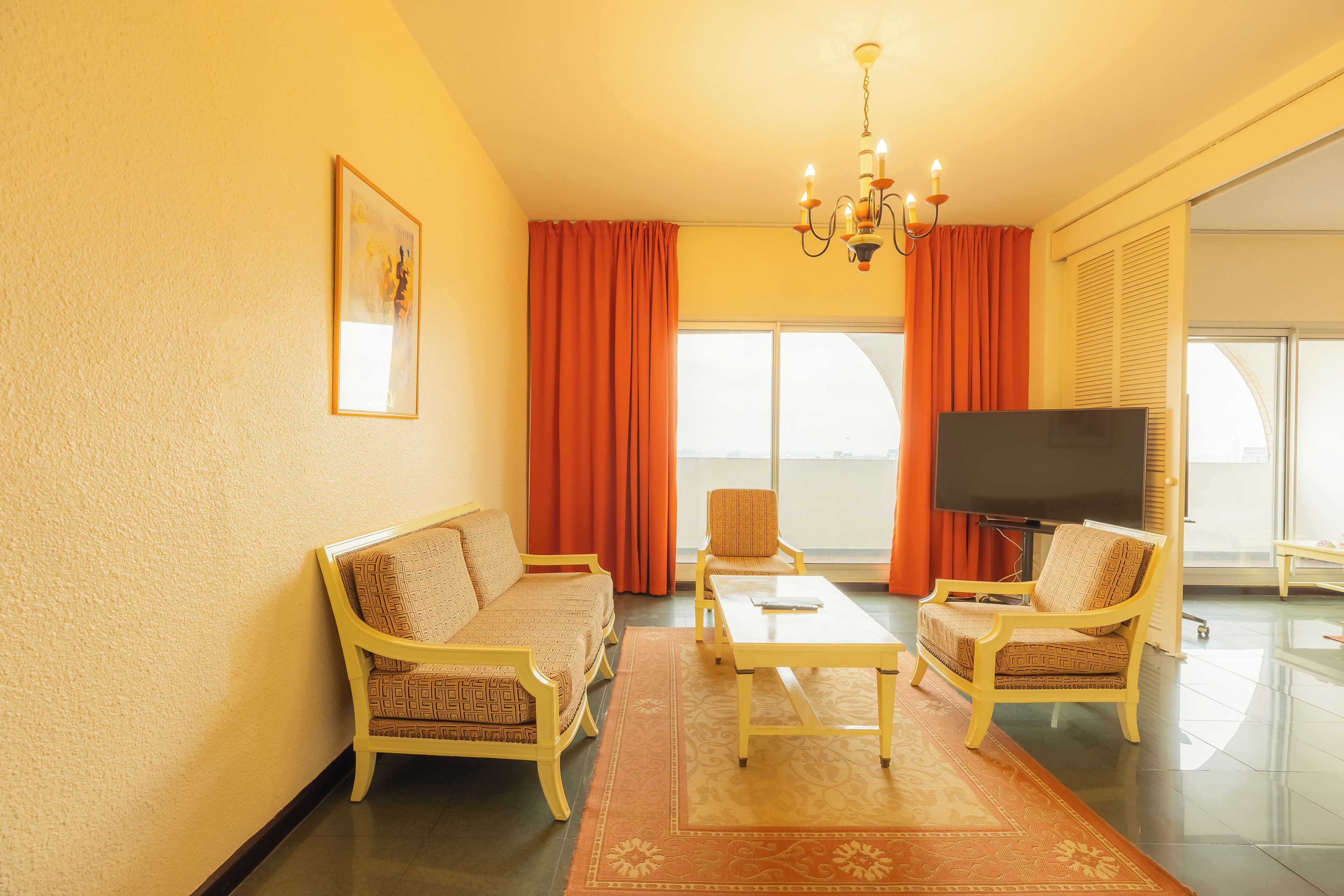 A living room with a sofa, armchairs, a coffee table, a TV, and a large window with curtains.