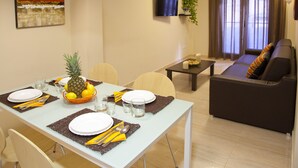 Un comedor con una mesa preparada para cuatro personas, un sofá, un televisor y una planta.