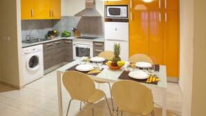 Een moderne keuken met een eethoek, met een wasmachine, magnetron en een fruitschaal op de tafel.