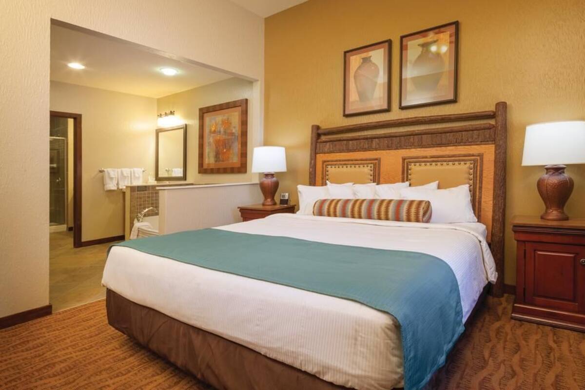 A hotel room with a large bed, two bedside tables with lamps, a headboard, and a mirror on the wall.