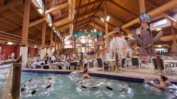 An indoor swimming pool with multiple lanes, wooden beams on the ceiling, and a large decorative tree sculpture. - Club Wyndham Glacier Canyon (Baraboo)