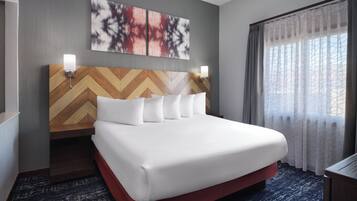 A hotel room with a large bed, a wooden headboard, two wall-mounted lights, and a window with sheer curtains.
