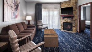 A modern hotel room with a stone fireplace, a large artwork of a deer head, a sofa, a chair, and a flat-screen TV mounted on the wall. - Club Wyndham Glacier Canyon (Baraboo)