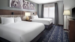 A hotel room with two beds, a headboard, a bedside table with a lamp, a large window with curtains, and a wall with bear artwork. - Club Wyndham Glacier Canyon (Baraboo)