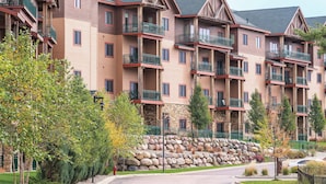 A multi-story hotel with balconies, stone facade, and a landscaped driveway. - Club Wyndham Glacier Canyon (Baraboo)