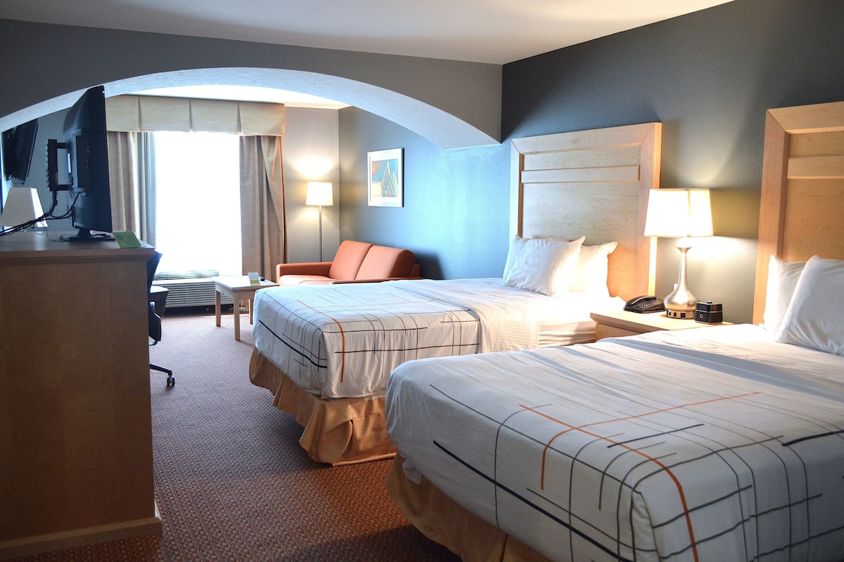 A hotel room with two beds, a desk, a chair, and a TV.