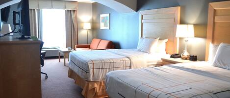 A hotel room with two beds, a desk, a chair, and a TV.