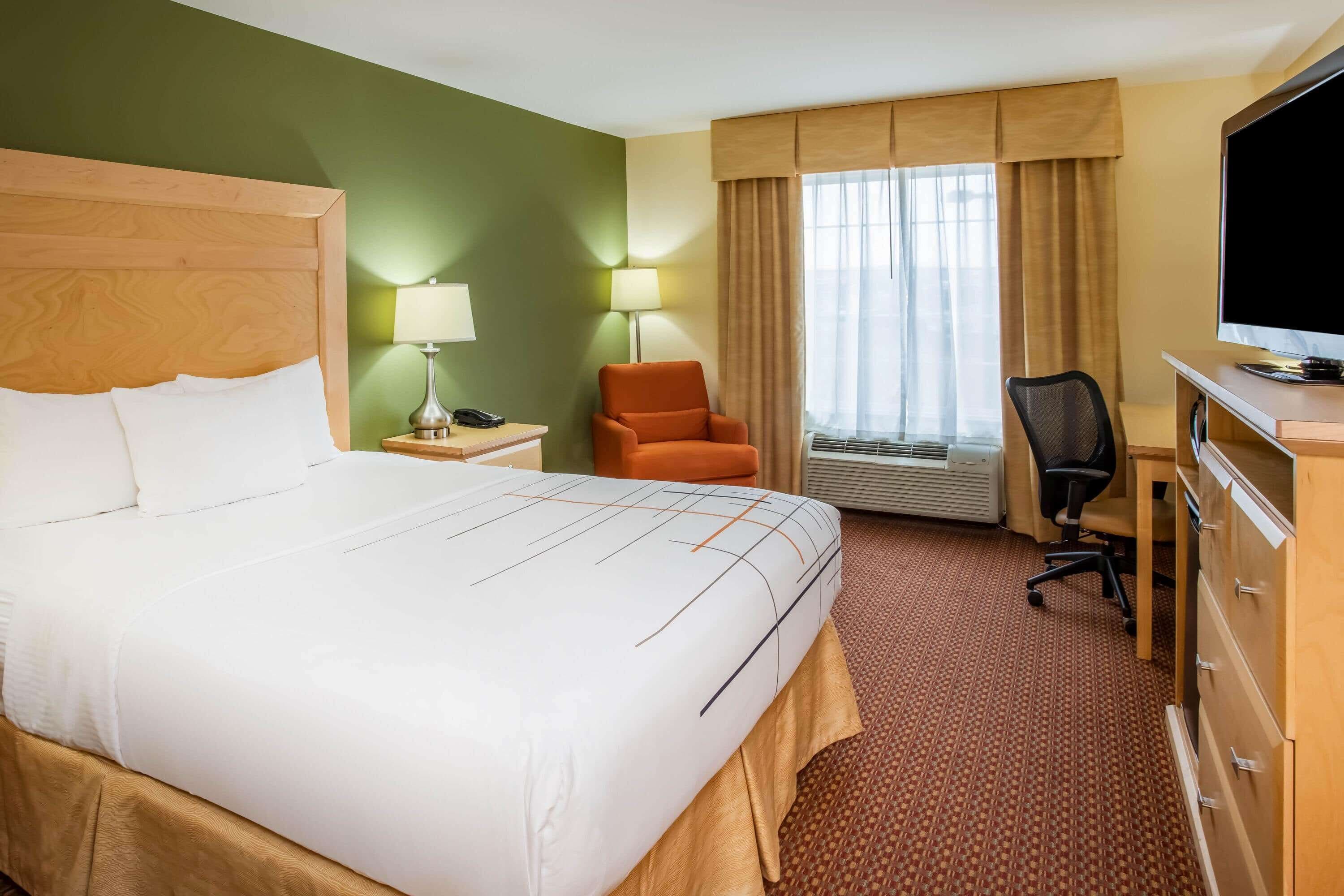 A hotel room with a large bed, a desk with a computer, a chair, a lamp, and a television.