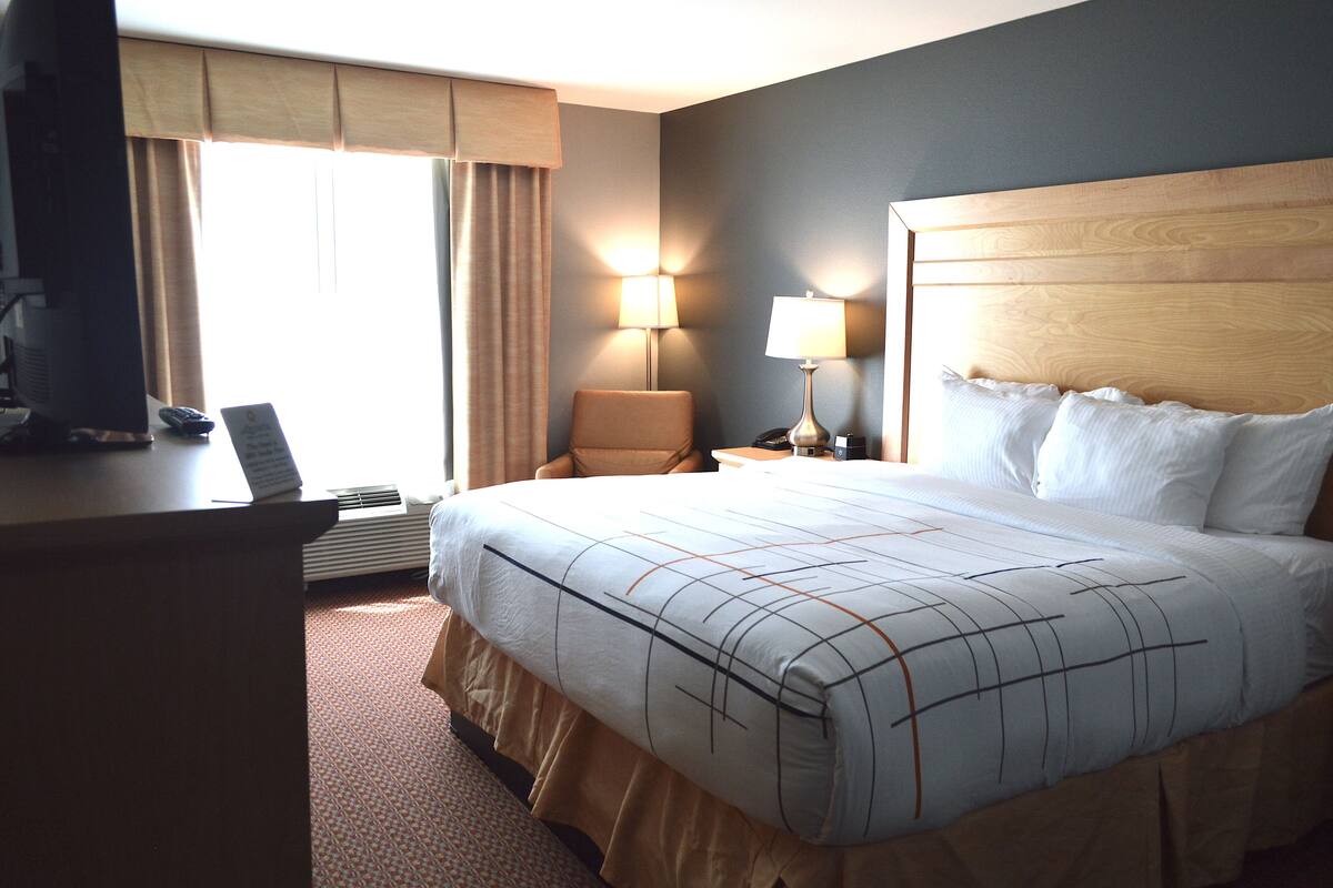 A hotel room with a large bed, a desk with a computer, two bedside lamps, and a window with curtains.