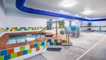 A modern indoor pool area with a colorful tiled border, a central pool, and a seating area with a potted plant.