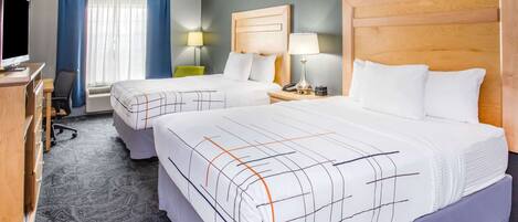 A hotel room with two beds, a desk, a chair, and a television.
