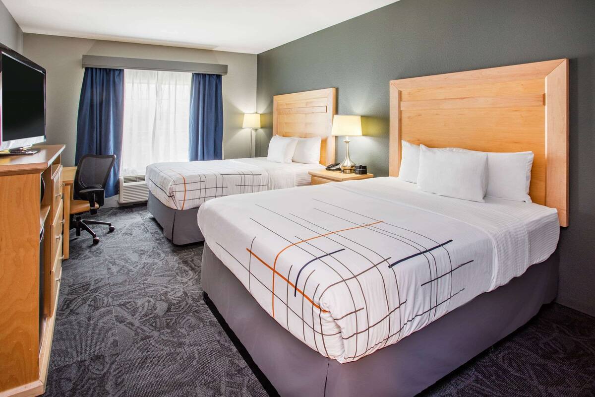 A hotel room with two beds, a desk with a TV, a chair, and a desk lamp.