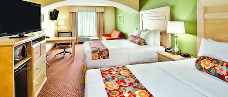 A hotel room with two beds, a desk, a television, and a small seating area.