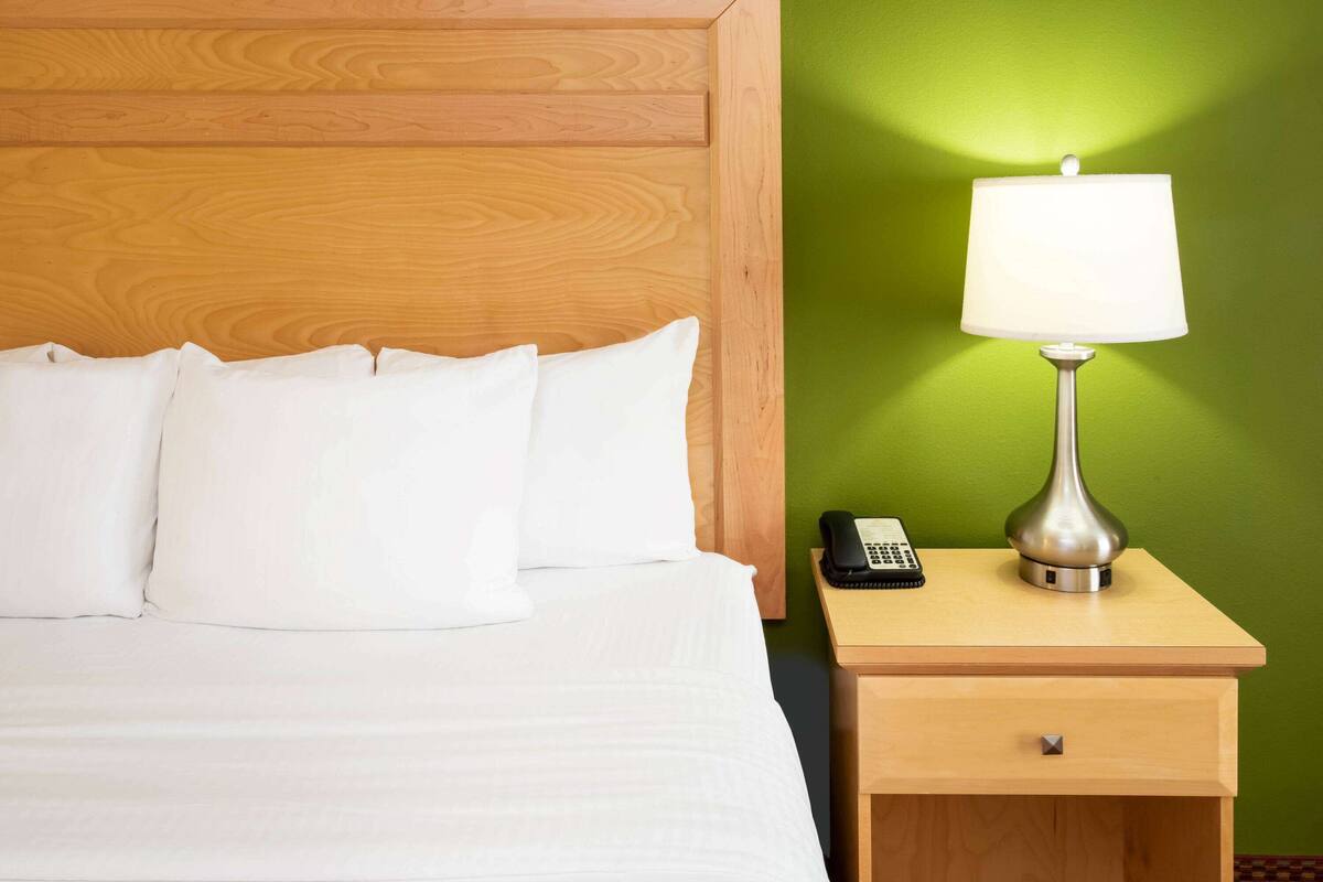 A hotel room with a wooden headboard, white bedding, a bedside table with a lamp, a telephone, and a green wall.