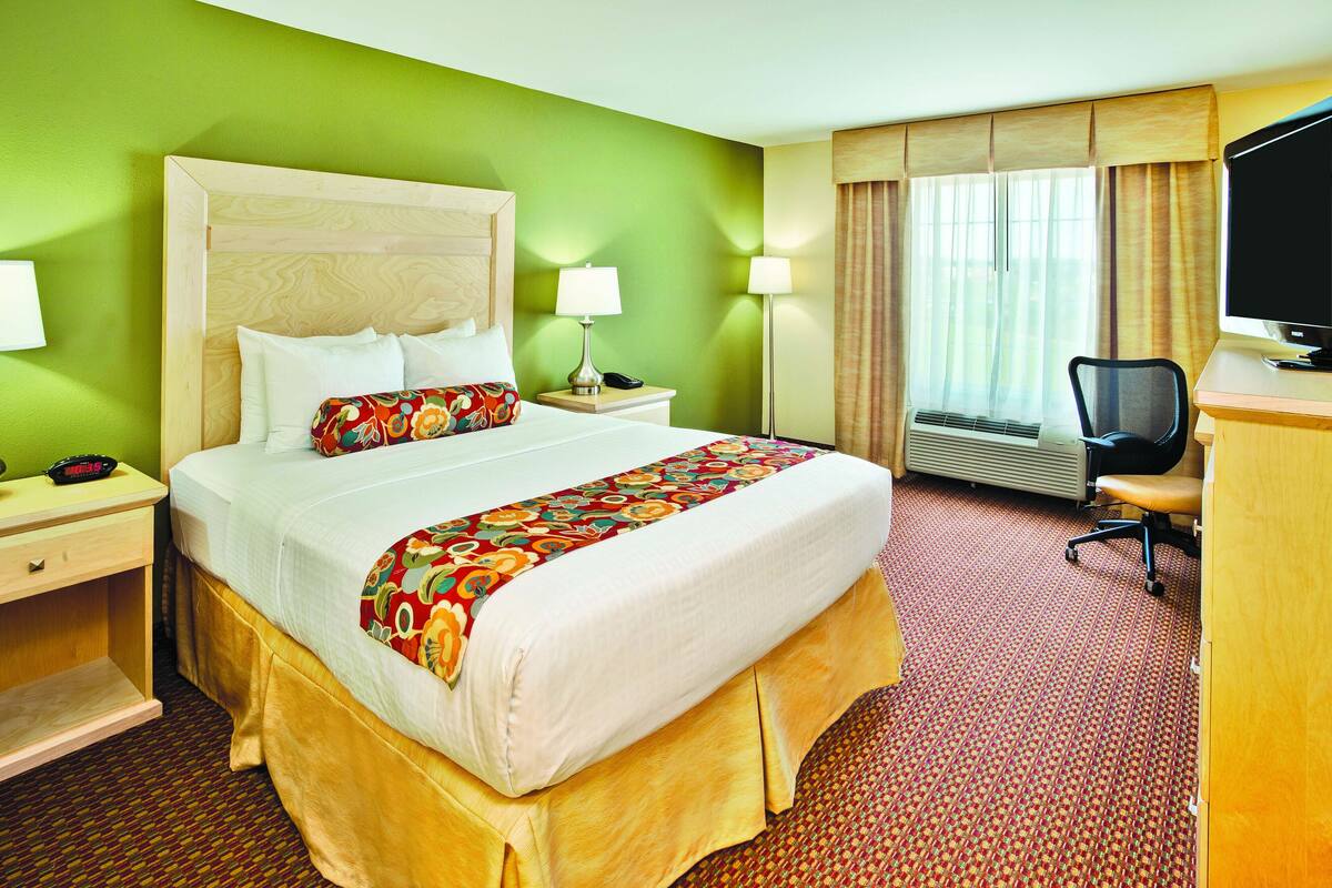 A hotel room with a large bed, a desk with a chair, a television, and a window with curtains.