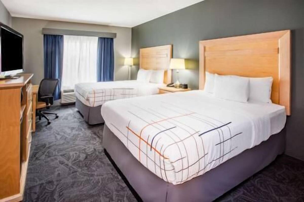 A hotel room with a large bed, a smaller bed, a desk with a computer, and a chair.