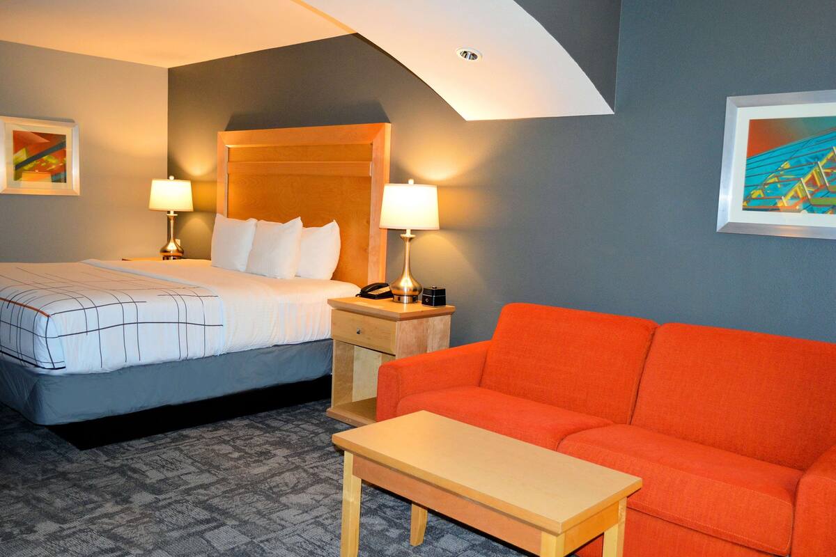 A hotel room with a bed, a nightstand, a table, a sofa, and two lamps.