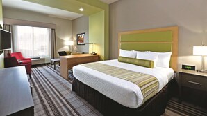 A hotel room with a large bed, a desk, a red chair, a TV, and a window with curtains. - La Quinta Inn & Suites by Wyndham Paducah (Paducah)