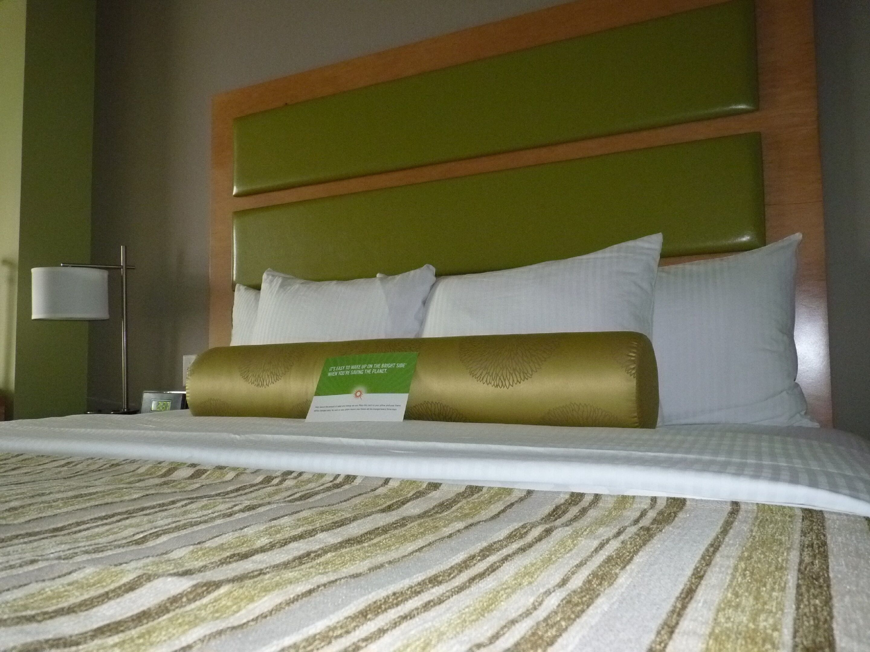 Una habitación de hotel con una cama bien hecha, un cabecero verde y una lámpara de noche.