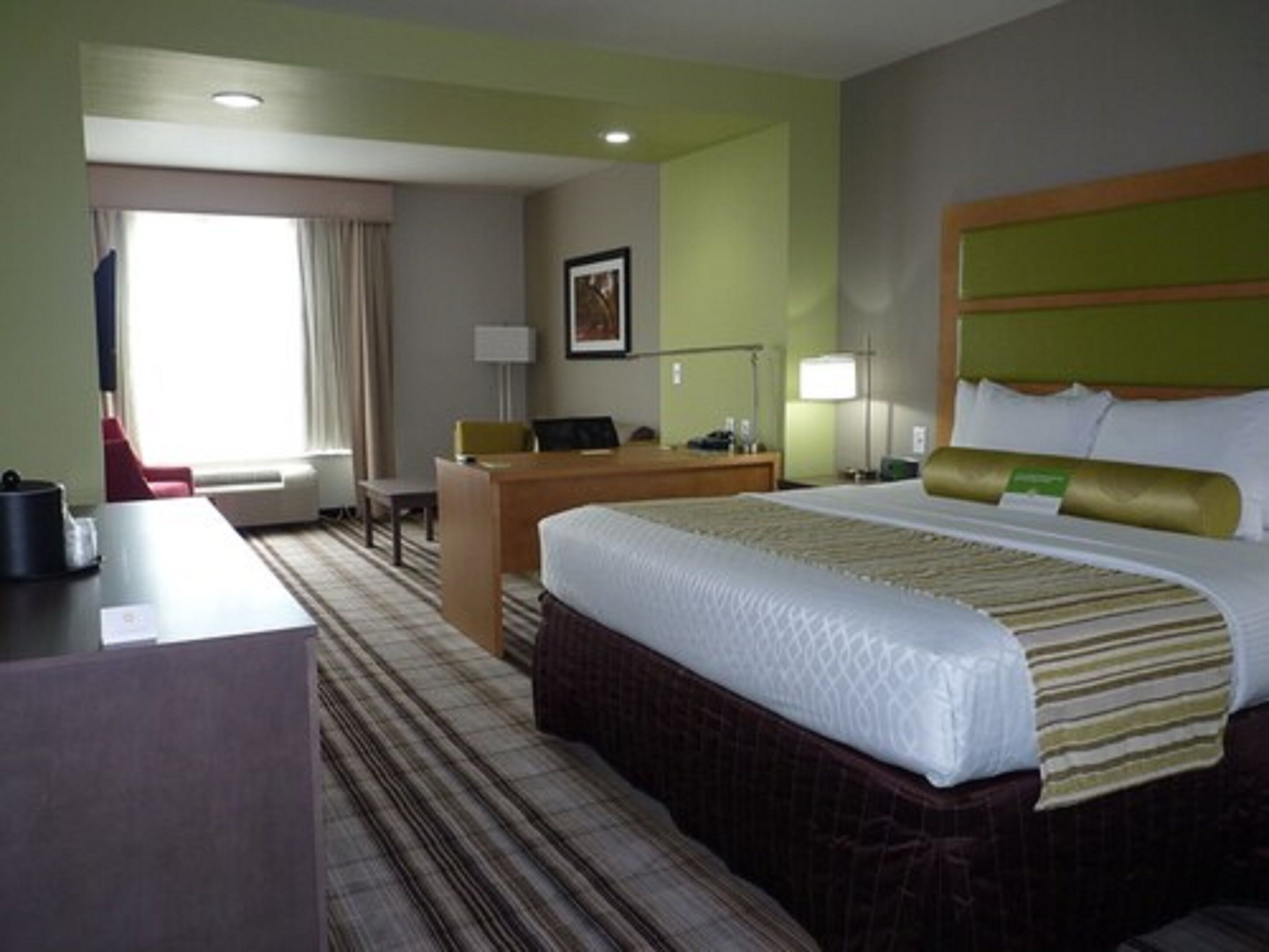 A hotel room with a bed, desk, chair, and a window with curtains.