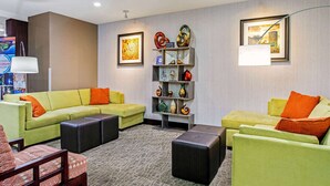 A modern hotel lobby with a sectional sofa, a small table, and a decorative shelf with vases. - La Quinta Inn & Suites by Wyndham Paducah (Paducah)