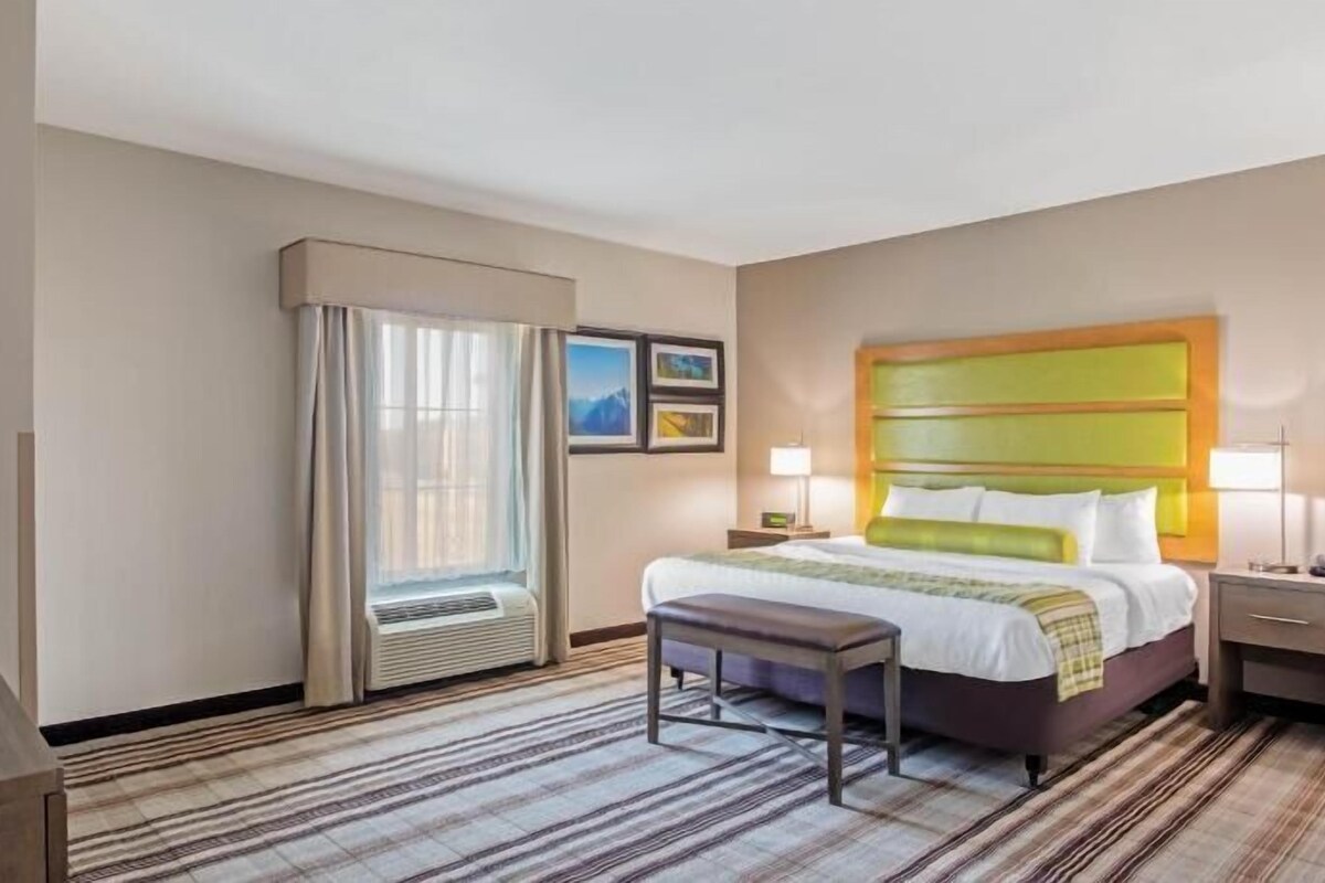 Une chambre d’hôtel équipée d’un lit, d’un bureau, d’une télévision, d’une fenêtre avec des rideaux et d’un climatiseur fixé au mur.