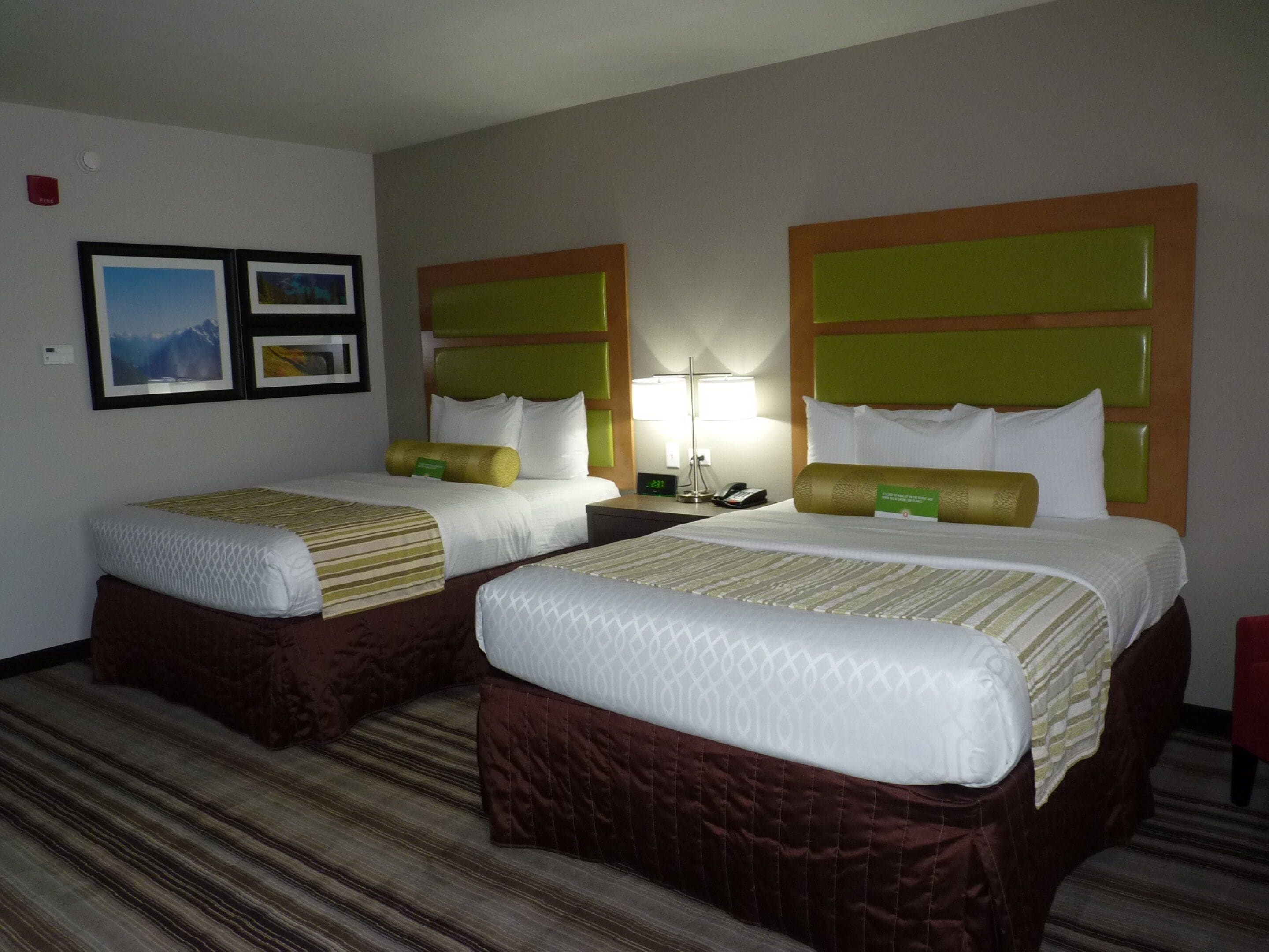 A hotel room with two beds, each with a headboard, a bedside table, and a lamp.