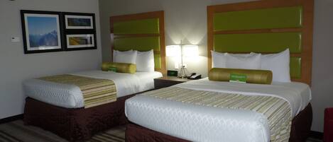 A hotel room with two beds, each with a headboard, a bedside table, and a lamp.