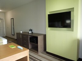Hotellihuone, jossa on sänky, työpöytä, jossa on kaukosäädin, kahvinkeitin, seinälle asennettu televisio ja ovi.