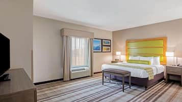 A hotel room with a bed, bedside table, lamp, and a television on a desk.
