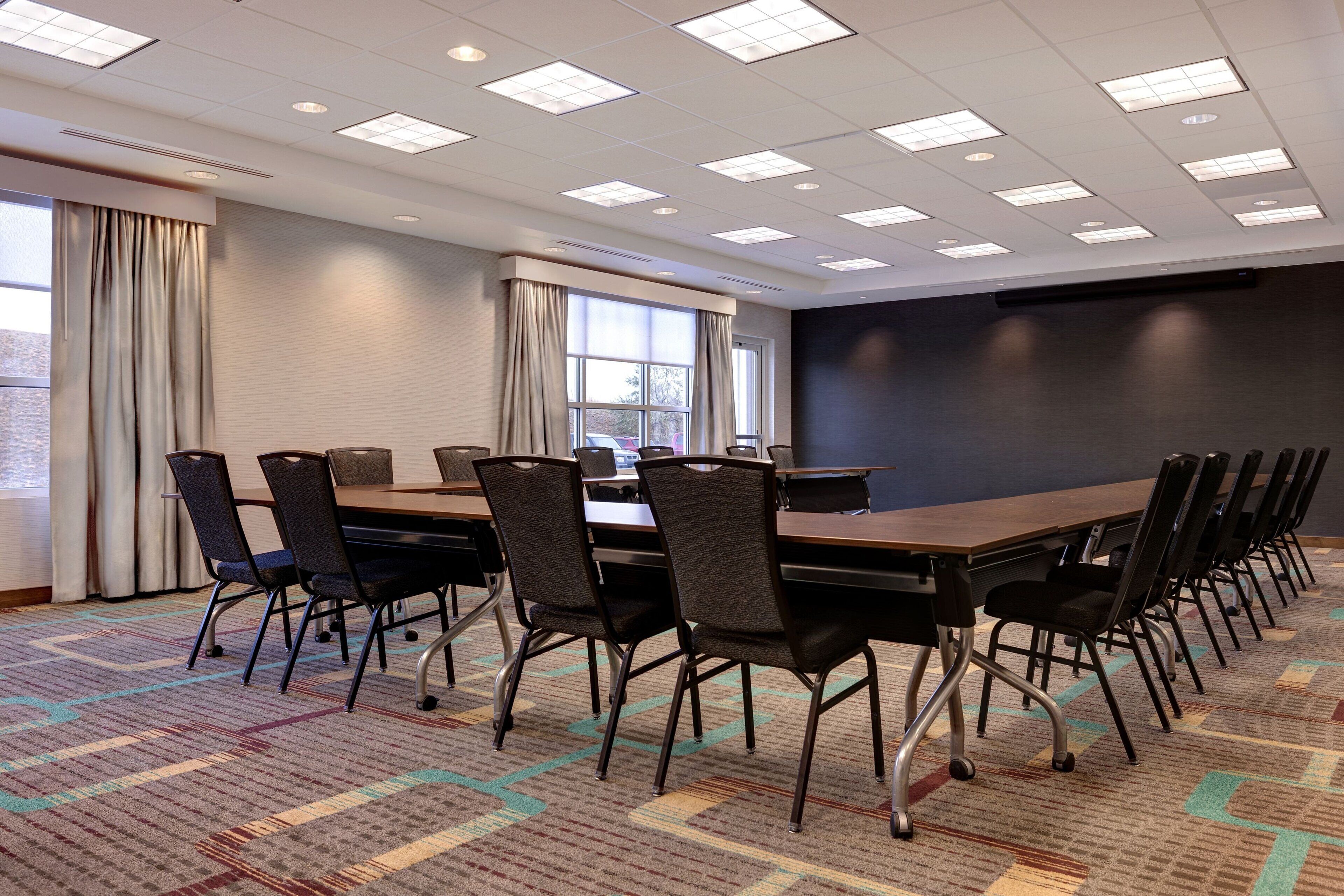 A conference room with a long table, chairs, a projector screen, and a large window with curtains.