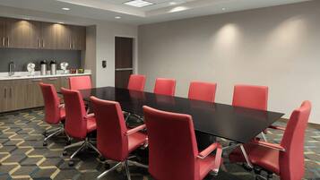A conference room with a black table and red chairs, a kitchen area with wooden cabinets, and a patterned carpet.