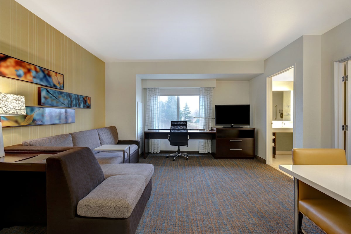 A hotel room with a sofa, a desk with a computer, a television, and a window with curtains.