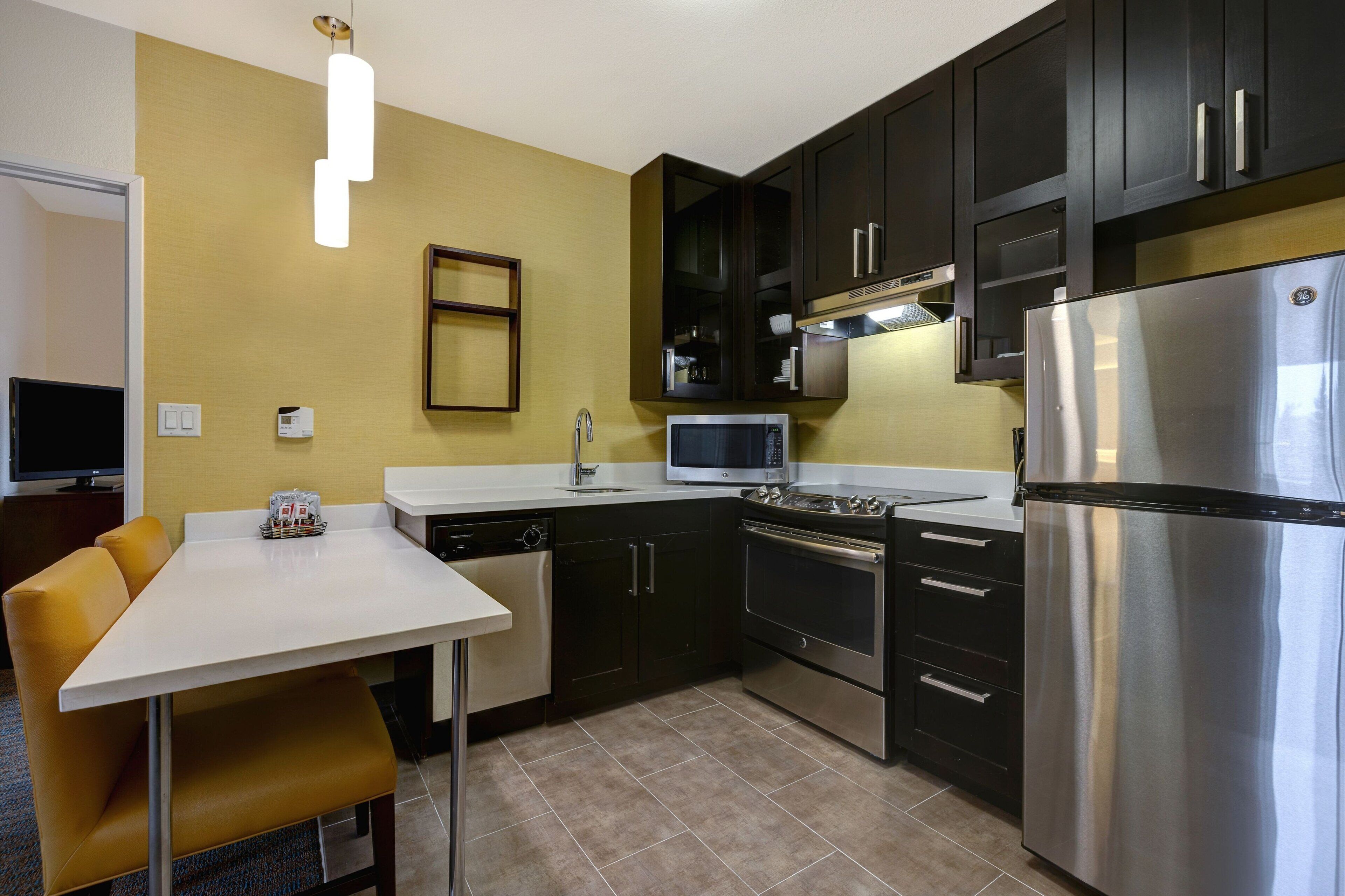A compact kitchen with dark cabinets, a stainless steel refrigerator, a microwave, and a dishwasher.