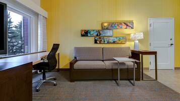 Een moderne hotelkamer met een bank, bureau, stoel en kunstwerk aan de muur.
