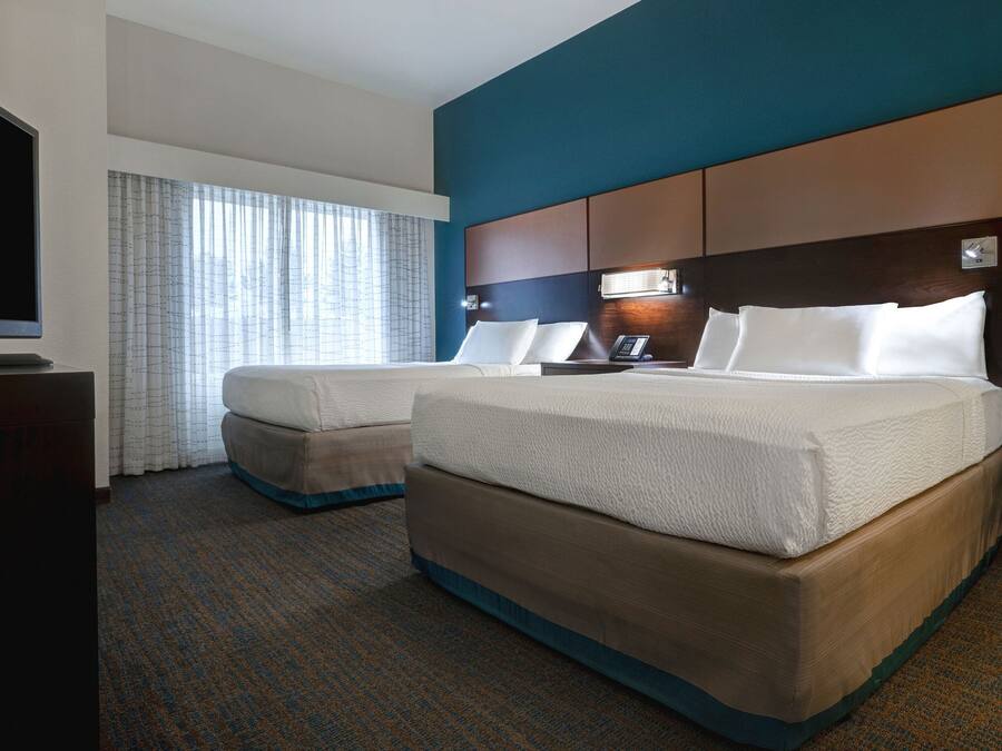 A hotel room with two beds, a TV, a desk, and a window with curtains.