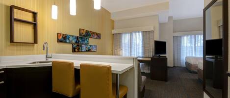 Una habitación de hotel moderna con cocina, una mesa de comedor con sillas, un televisor y un espejo grande.