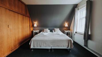 Una habitación de hotel con una cama grande, dos lámparas de noche, un ventanal con cortinas y un armario de madera.