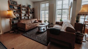 Un salón acogedor con un sofá de cuero marrón, una mesita de centro y una estantería llena de libros y objetos decorativos.