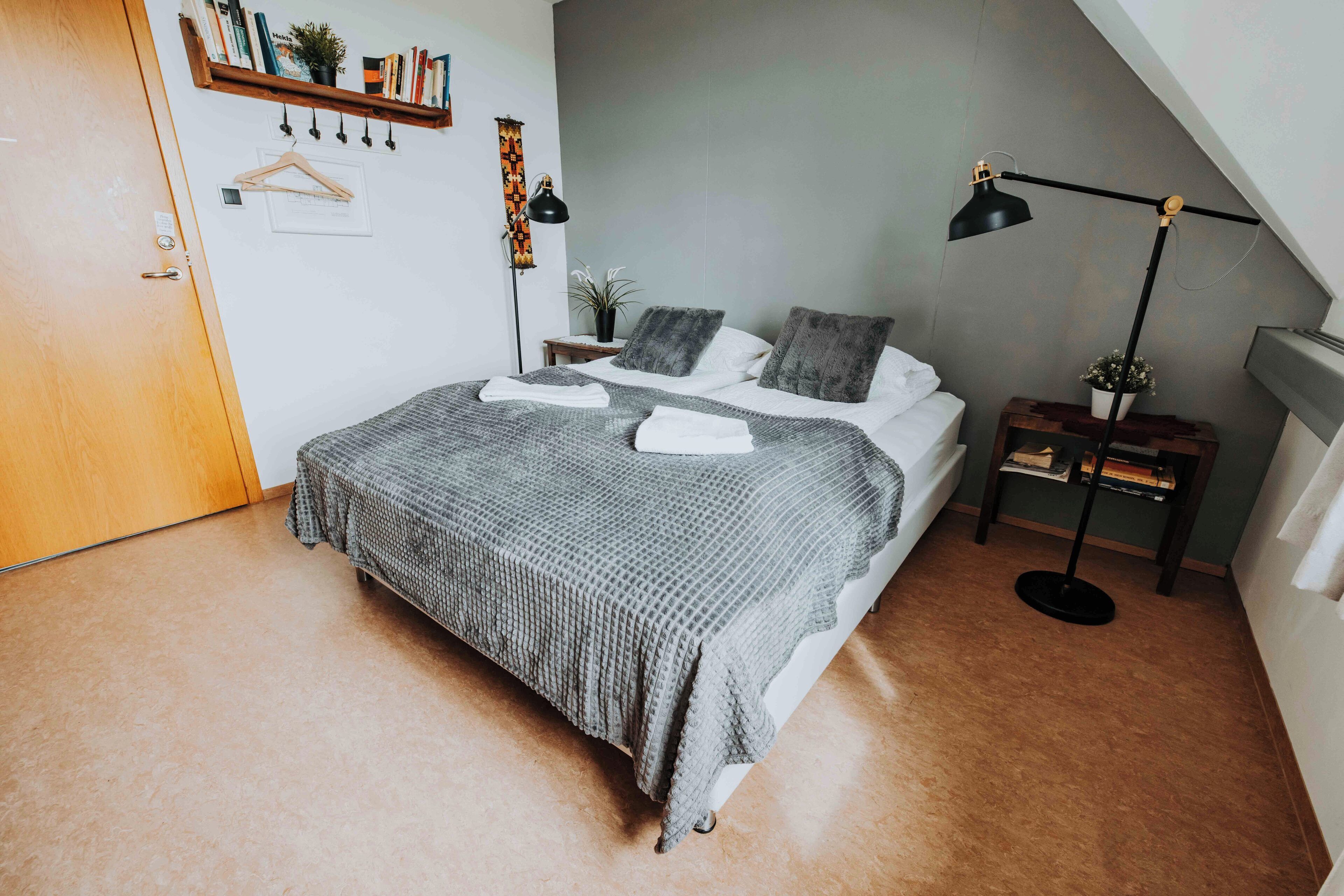A bedroom with a bed, a bedside table, a floor lamp, and a bookshelf.