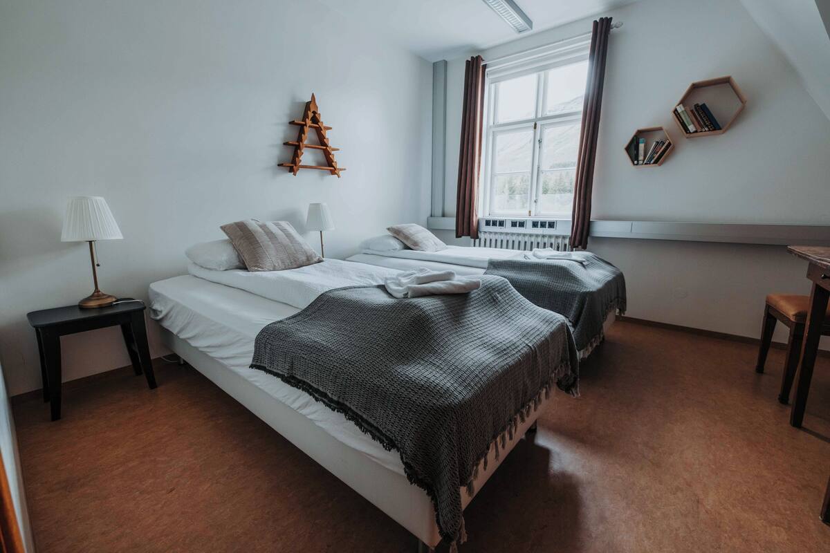 A bedroom with two beds, a standing lamp, a ladder, and a window with curtains.
