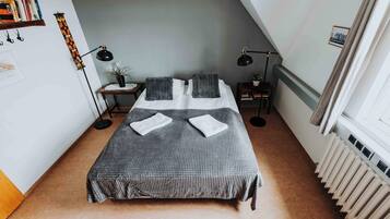 A neatly arranged bedroom with a bed, two bedside lamps, a small table with a plant, and a radiator.