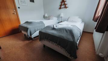 A room with two single beds, each with a bedside table and lamp, a wooden ladder on the wall, and a radiator on the right.