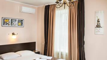 Una cama bien hecha con sábanas blancas y una manta marrón, un aire acondicionado de pared, una lámpara de pared y un candelabro.