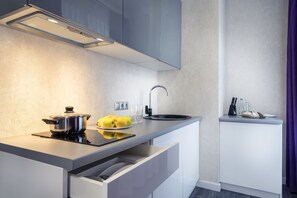 A modern kitchen with a built-in stove, a sink, and a countertop with a pot, lemons, and glasses. - Hotel Status Apartments (Kyiv)